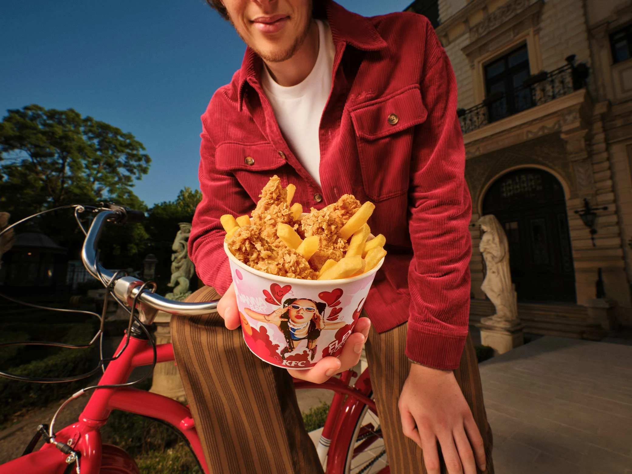 osoba drži kfc bucket s hrskavom piletinom i pomfritom pored bicikla u gradu