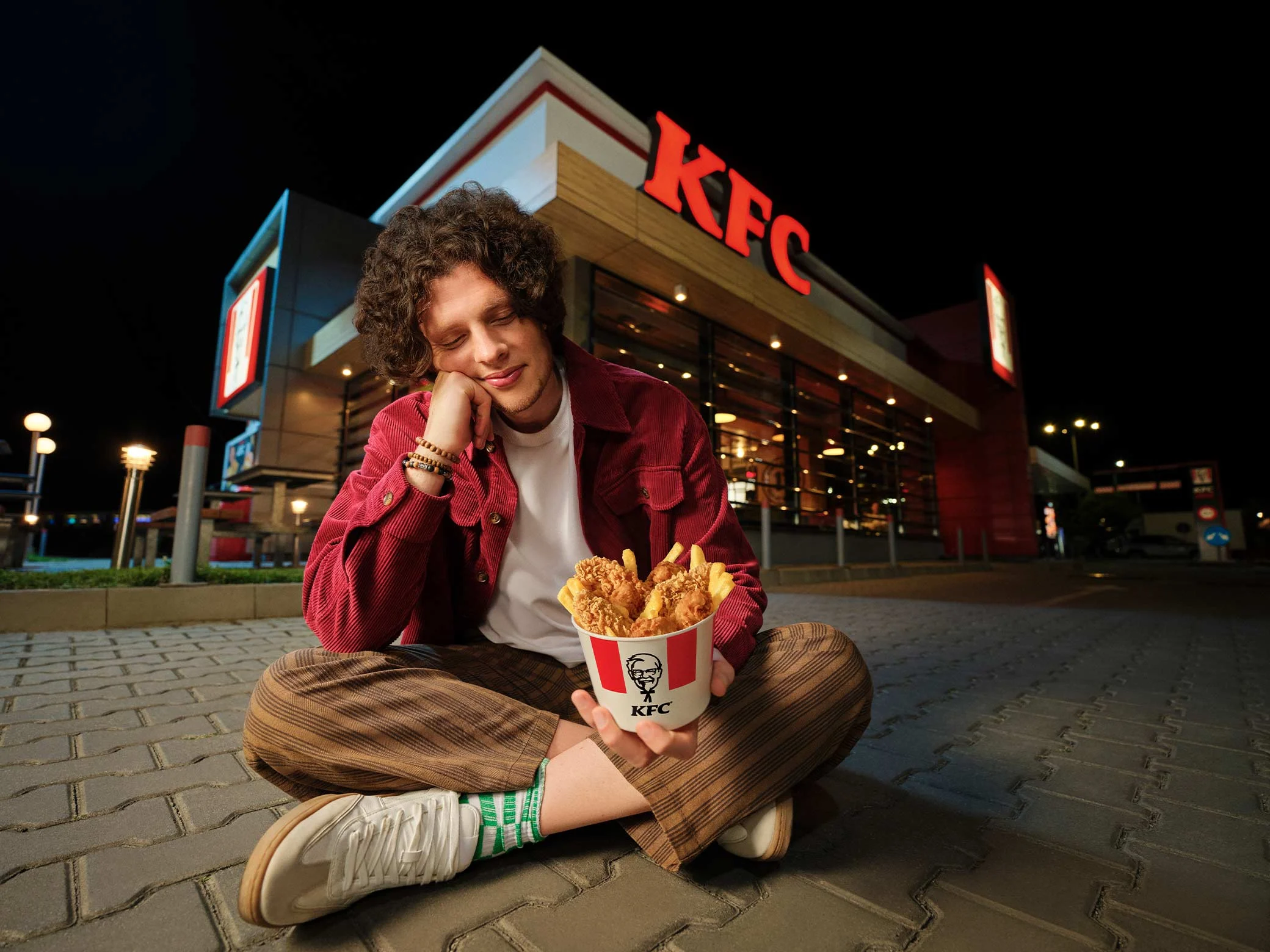 osoba sjedi ispred kfc restorana i drži bucket sa hrskavom piletinom